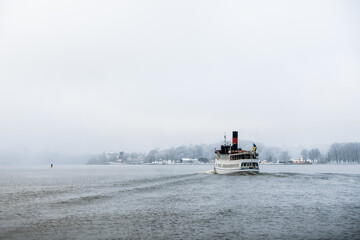 Steamboat with red chimney cruising on a foggy winter day in Stockholm, Sweden as seen from the rear