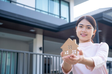 Young Asian woman holding wooden house shape  with the village background, New house, House insurance, Real Estate or Housing Loan concept.