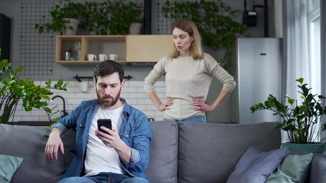 Irritated young woman finds message of infidelity on the husband phone hitting him and demands to explain Perplexed bearded man feels confused while his wife screaming at him Cheating lie concept 