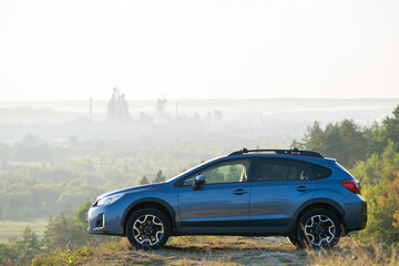 Blue off road car at dawn on grassy hill on distant foggy city landscape background. Extreme travel...
