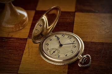 An antique gold pocket watch lies on a chess board