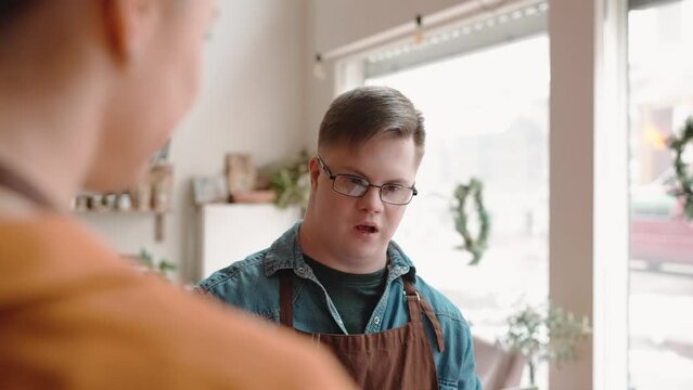 Cute man waiter with Down syndrome talking to a girl colleague in the cafe