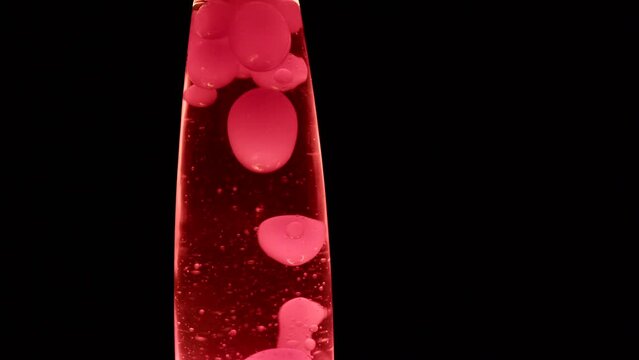 Close macro shot of red lava lamp. Moving doubles of hot red wax inside a lava lamp in front of black background.