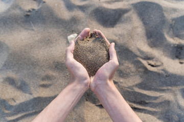 Young man hands pholding sand at the beach. Upper view