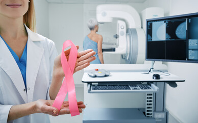 Mammologist showing breast cancer awareness ribbon in mammography room, urging women to have...