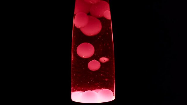 Close macro shot of red lava lamp. Moving doubles of hot red wax inside a lava lamp in front of black background.