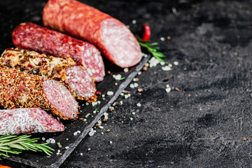 An assortment of delicious salami sausage on a stone board with rosemary. 
