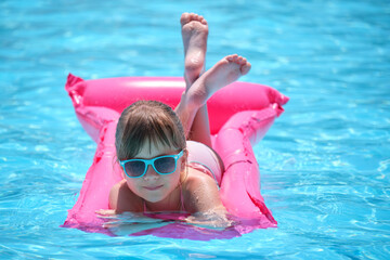Happy child girl relaxing on inflatable air mattress in swimming pool on sunny summer day during...