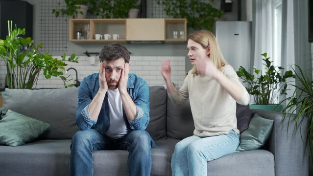 Irritated young woman screams in frustration offends abases her stressed disappointed husband in the living room at home Domestic psychological violence and emotional abuse against man