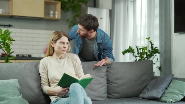Domestic violence Family conflict A man shouts and beats a woman at home Frightened woman closes her arms, sitting on the couch. She is afraid Psychological emotional abuse