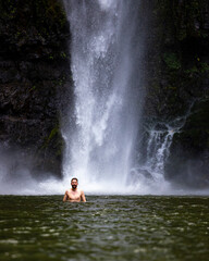 Fototapeta na wymiar A man stands in the water beneath the mighty nandroya falls in wooroonooran national park in queensland, australia; swimming in a waterfall in the atherton tablelands