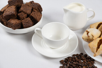 Empty coffee ceramic cup with milk jug, chocolate cake and coffee beans on a white background