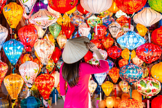 Young female tourist in Vietnamese traditional dress looking at Paper ornamental lanterns in Hoi An Ancient town