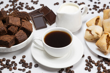 Delicious breakfast - aromatic coffee in a cup, milk jug, chocolate and cake cubes.