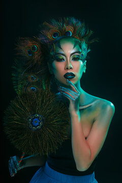 Beautiful Asian girl with creative makeup in the form of a peacock on a dark background.
