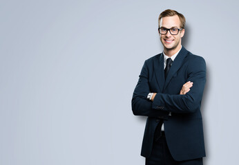 Obraz na płótnie Canvas Portrait of businessman in eye glasses, spectacles, black suit and tie, with crossed arms, against grey color background. Business concept. Smiling man at studio picture. Copy space for ad.