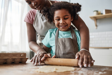 Loving mother and daughter baking together at home and rolling dough