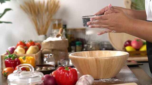 woman standing in the kitchen and using the sieve, sifting the flour. which is the process of making pizza. to food and pizza homemade concept.