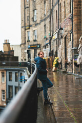 Victoria Street in Edinburgh, the rain drenching his coat as he gazes down the bustling street....