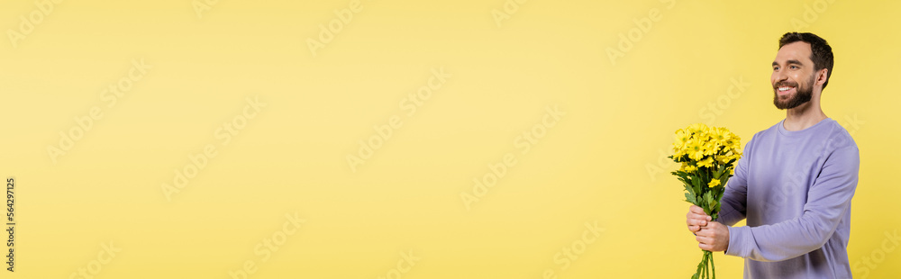 Wall mural cheerful bearded man holding bouquet and looking away isolated on yellow, banner. - Wall murals