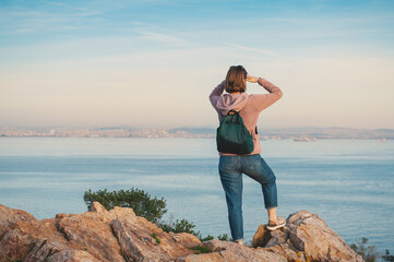 Young beautiful woman looking on the sea stand on the rock