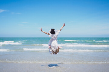 Happy young lady are jumping, feel relax, fun, and enjoy holiday at tropical coast beach with clear cloud and blue sky background