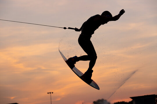 Silhouette Wakeboarder making tricks on sunset, Young surfer wakeboarding in the cable park, Extreme athlete having fun wakeboarding.