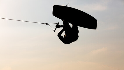 Silhouette Wakeboarder making tricks on sunset, Young surfer wakeboarding in the cable park,...