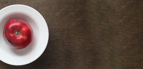 beautiful red apple in a white plate on a dark wooden surface, space for text