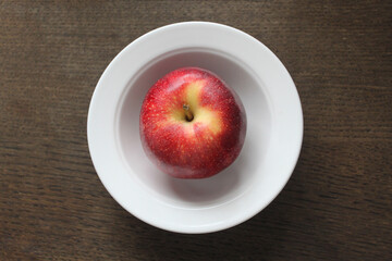 beautiful red apple in a white plate on a dark wooden surface