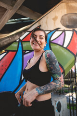 Rude, sexy, beautiful, happy and tattooed young girl smiling with black crop top in front of a colorful graffiti