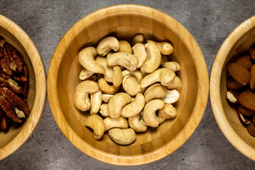 Wooden bowl with roasted cashew nuts on a slate table. Top view, series photo with other dried fruits.