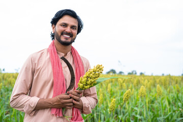 Happy smiling young farmer holding crop and sickle by looking camera at corn or maize field - concept of real rural people, happiness and cultivation © WESTOCK
