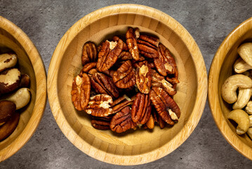 Wooden bowl with roasted pecans on a slate table. Top view, series photo with other dried fruits.