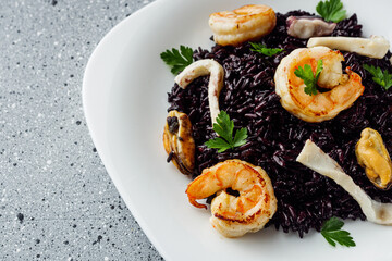 delicious black rice with shrimps and seafood on a gray stone background