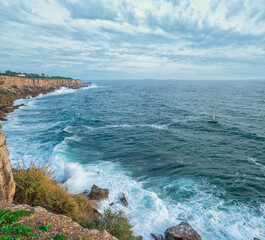 Obraz premium Beautiful cloudy sky and foaming waves approaching rocky shore of the Atlantic ocean. Beautiful nature background of Portugal.