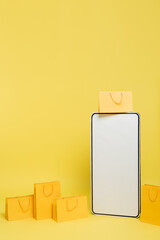vertical view of huge mock-up of smartphone near shopping bags on yellow background.