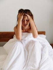 Woman sadness sits on the bed in the bedroom and covers her body with a blanket, early awakening, sleepy look, hangover, fatigue and depression