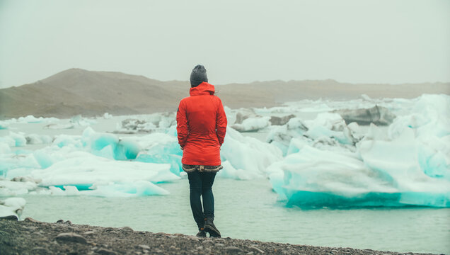 Back view of young woman standing in ice lagoon and looking on blue iceberg, exploring the glacier in Iceland.