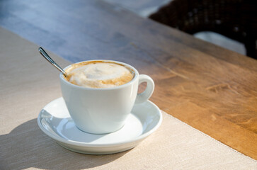 Cappuccino coffee in white cup on wood table.