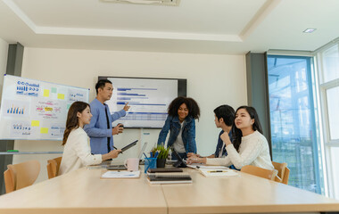 Group of Asian business people brainstorming at a meeting to start a new business. In a small office with a laptop and financial graphs on the table