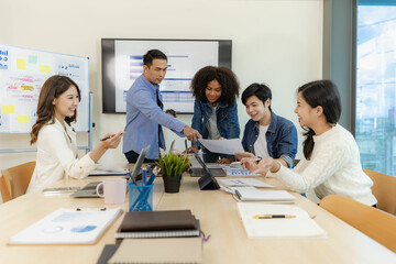 Group of Asian business people brainstorming at a meeting to start a new business. In a small office with a laptop and financial graphs on the table
