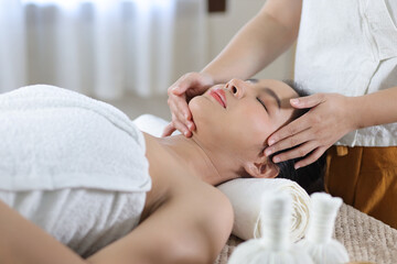 Relaxed Asian woman receiving beauty massage in spa salon.