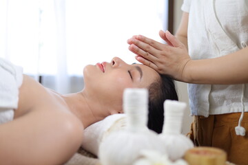 Young woman enjoying massage in spa salon. Masseur doing massage the head of an Asian woman in the spa salon.