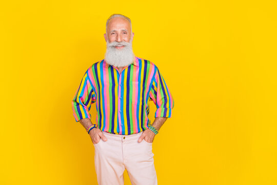 Photo of good mood handsome retired man with white beard dressed striped shirt hold arms in pockets isolated on yellow color background