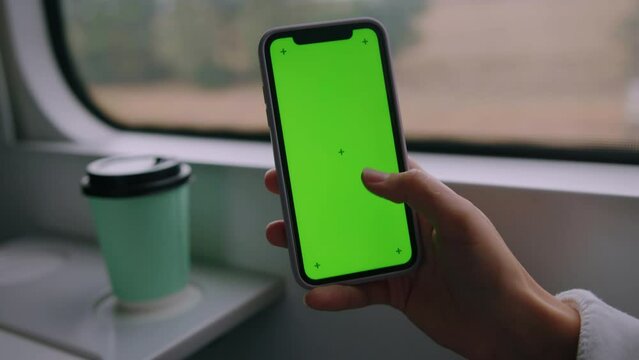 The hand of a woman holding a mobile phone with a green screen on the background of a train car