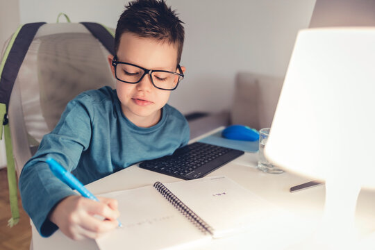 Cropped shot of cute little boy with glasses sitting at the table, doing homework, using computer at home.