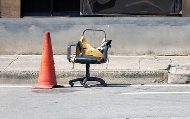 The damaged office chair beside a cone for traffic restriction on the street