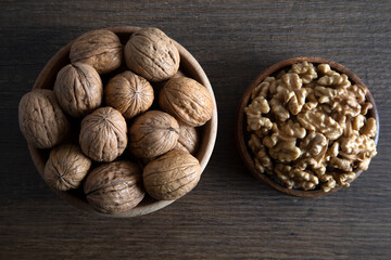  Peeled walnuts and whole walnuts in wooden bowl,top view