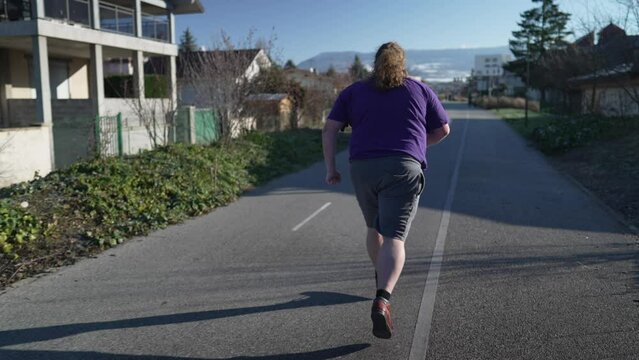 Back of one overweight man running outside in street. A fat person getting back into shape. Motivational concept